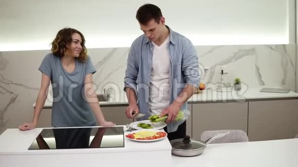 明亮的白色厨房里有一对快乐的情侣他们在平底锅上准备了煎蛋卷一起上菜在上面加入切碎的芹菜视频的预览图