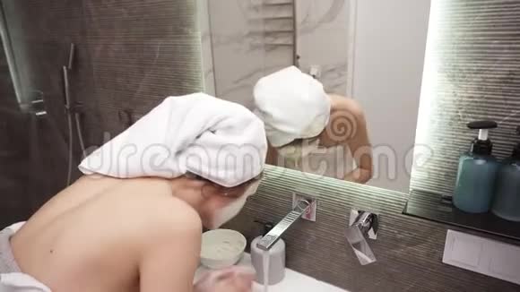一个女人站在洗手池附近用白毛巾洗下了一个带水的白色化妆面具视频的预览图