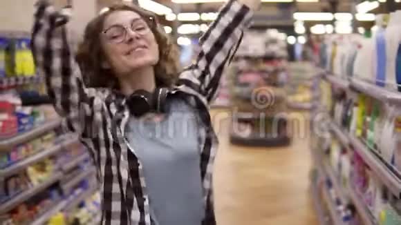 特写一幅年轻女子的肖像她穿着格子衬衫戴着眼镜站在杂货店的过道上跳舞兴奋微笑视频的预览图