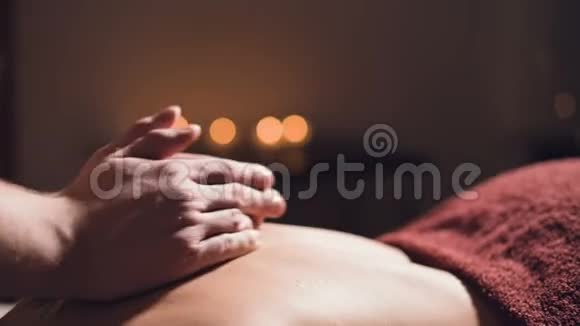 年轻的男性按摩治疗师在按摩室里给有纹身的女人做背部按摩按摩室里灯光昏暗视频的预览图