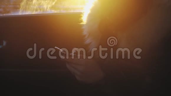 剪影女孩在日落时驾驶汽车时使用智能手机视频的预览图