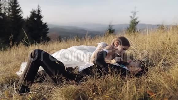 新婚夫妇白人新郎和新娘躺在山坡上的草地上视频的预览图