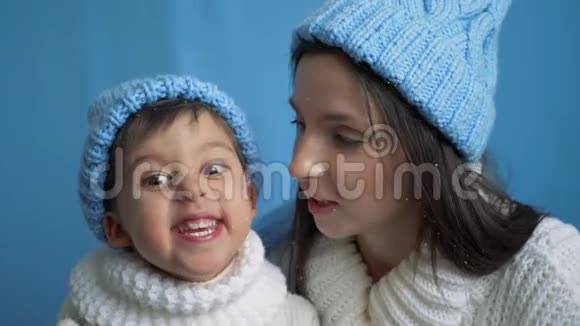 母亲和儿子穿着蓝色针织暖和帽子穿着白色毛衣在雪地里视频的预览图