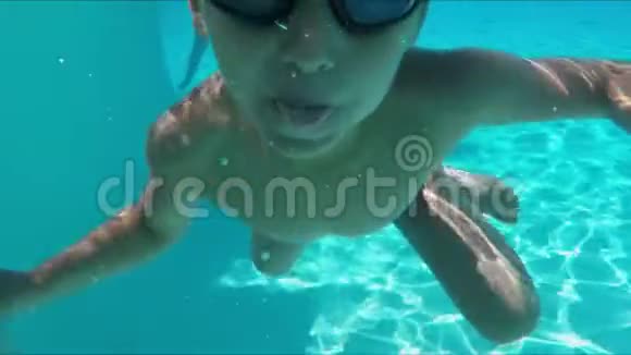 男孩在游泳池里潜入水中开始做鬼脸露出舌头视频的预览图