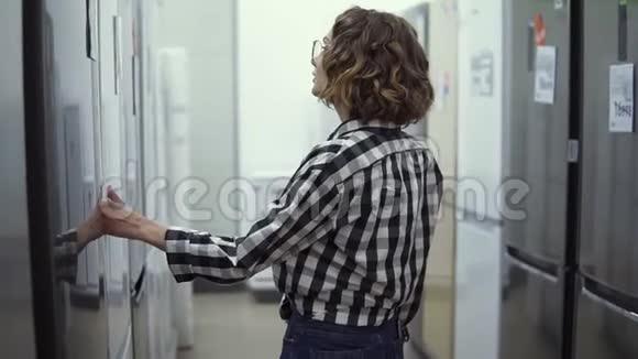 开朗的年轻女孩在超市挑选家用冰箱穿格子衬衫的卷发女士决定买一件新的视频的预览图