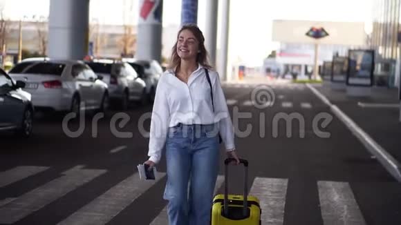 兴奋时尚的女人带着手推车走黄色的箱子在空的机场航站楼外面的路上苗条的女性穿着视频的预览图