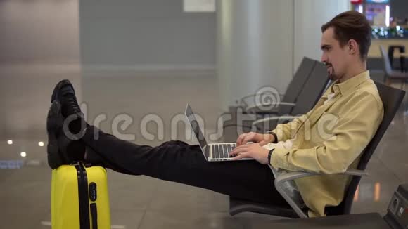 一个留胡子的年轻人坐在机场等待飞机起飞用笔记本电脑有个视频视频的预览图