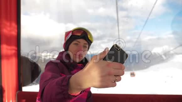 有魅力的年轻女子在一个滑雪胜地站在雪地上用手机视频的预览图