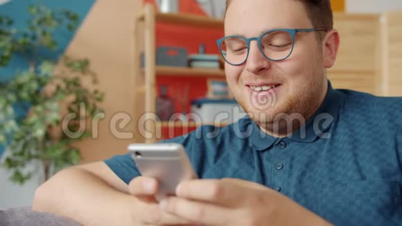 快乐的男人拿着智能手机触摸屏在家里微笑视频的预览图