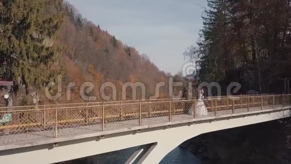 新婚夫妇新娘和新郎在一座山河上的桥上空中景观视频的预览图