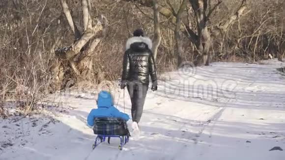 妈妈带着一个孩子坐在雪覆盖的森林上的雪橇上开朗的寒假观念视频的预览图