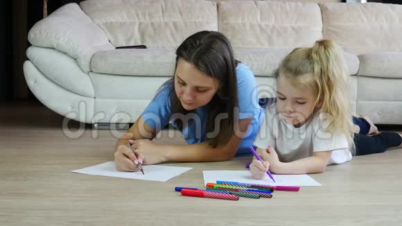 年轻的母亲画着彩色图画可爱的女儿躺在温暖的地板上视频的预览图