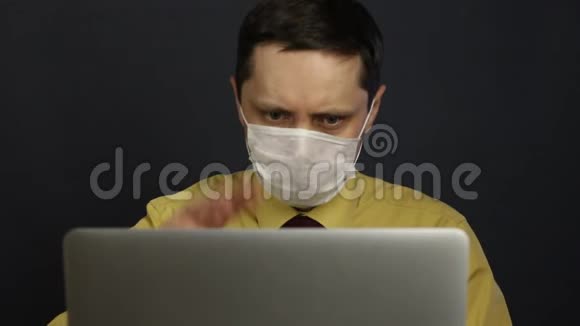 一个戴着医疗面具的男人坐在笔记本电脑前通过互联网参与交流手势广泛显示视频的预览图