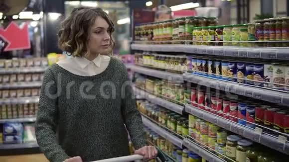 特写白种人的女人拿着一辆手推车走在商店货架附近在杂货店市场上检查一个玻璃瓶女性客户视频的预览图
