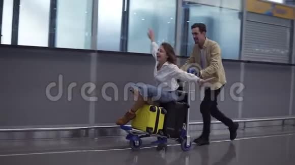 有趣的一对在机场迷人的年轻女子和英俊的男人带着手提箱准备旅行玩得开心视频的预览图