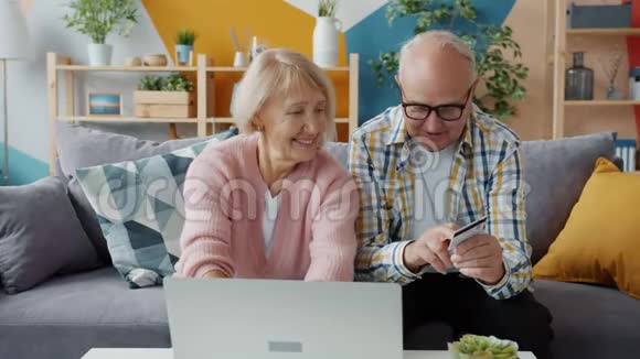 在家使用笔记本电脑用银行卡在线支付的快乐老人视频的预览图