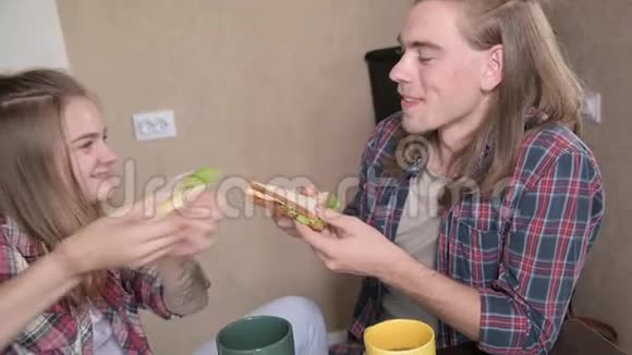 可爱的年轻夫妇坐在厨房里吃三明治微笑着特写视频的预览图
