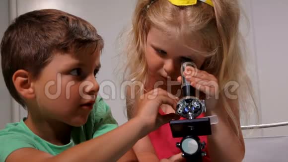 小男孩向一个可爱的小女孩展示如何透过显微镜看视频的预览图