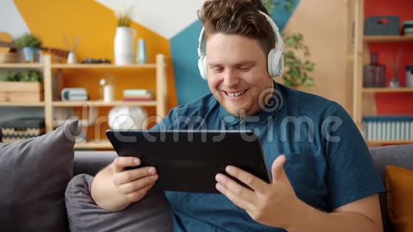 帅哥在家戴着耳机在平板电脑屏幕上欣赏视频视频的预览图