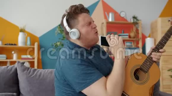 在家戴着耳机的智能手机中男人弹吉他唱歌的慢动作视频的预览图