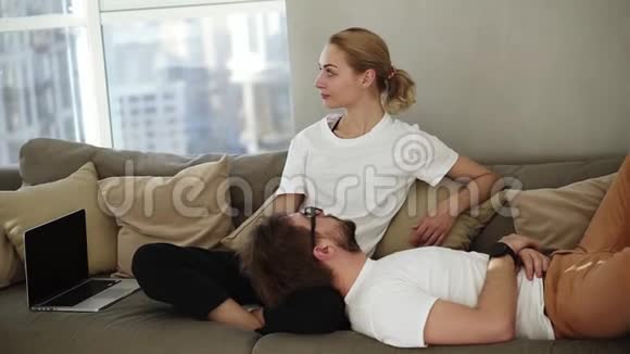 放松的夫妇在沙发上放松一起享受他们的关系当男人躺着的时候金发女人站在一边视频的预览图