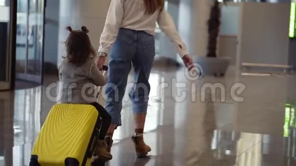 机场候机楼年轻的无法辨认的母亲骑着她可爱的女儿在一个小黄色的手提箱妈妈是黄色的视频的预览图