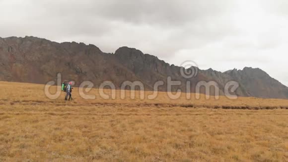 一对戴着帽子和太阳镜的大背包的旅行者男女在高山上漫步的鸟瞰图视频的预览图