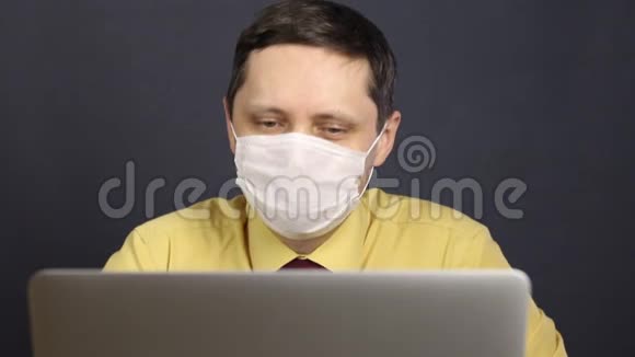 一个戴着医疗面具的人用笔记本电脑读新闻笑眯着眼睛冠状病毒流行期间的自我隔离视频的预览图