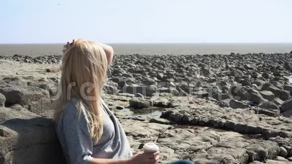 一个女人坐在海滩上看着远处的鸟儿向大海望去视频的预览图