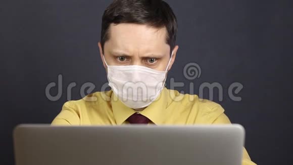 一个戴着医疗面具的人用笔记本电脑读新闻他专注地盯着屏幕若有所思地挥动着头自我孤立视频的预览图