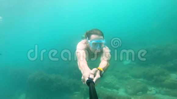戴面具的肌肉男在水下游泳拿着相机在前面特写镜头视频的预览图