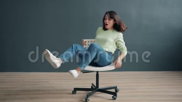 无忧无虑的女士在工作室的椅子上旋转享受有趣的活动视频的预览图
