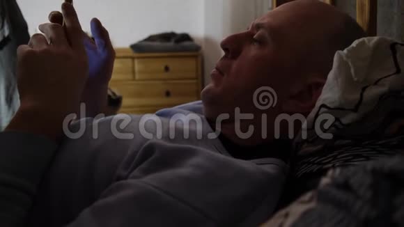 男人躺在床上拿着智能手机滚动社交媒体信息视频的预览图