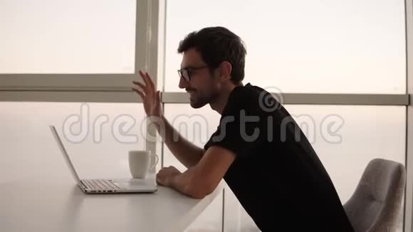穿着时尚眼镜手提电脑有视频通话的白种人放松穿着黑色衣服的笑容开朗的男人视频的预览图