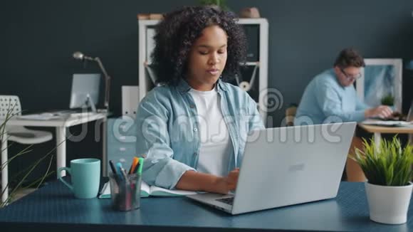 年轻的非洲裔美国女士在办公室里使用笔记本电脑同事在后台工作视频的预览图