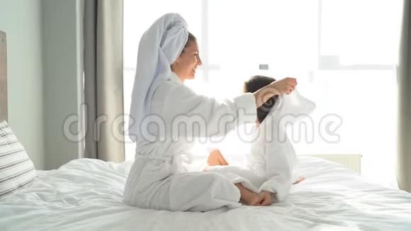 年轻可爱的母亲和女儿穿着晨衣洗澡后拥抱在一张大床上视频的预览图