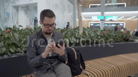 携带背包和移动设备的旅客机场休息室视频的预览图
