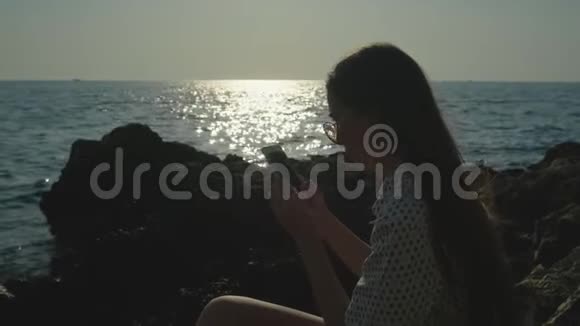 女人手里拿着智能手机坐在石海岸视频的预览图