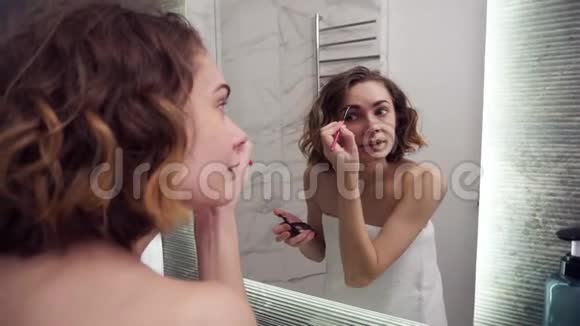 漂亮的女人用眉毛铅笔在镜子里化妆快乐的女性使用美容化妆品来提高自己视频的预览图