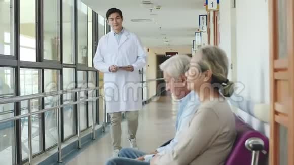 年轻的亚洲医生在医院走廊上和老两口说话视频的预览图