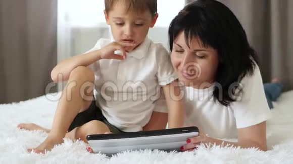 家庭幸福母亲和孩子躺在沙发上用平板电脑玩或上网协作视频的预览图