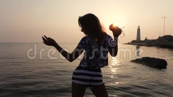 穿着短裤的运动女孩摇动着臀部在大海和日落的背景下跳舞手里拿着一根音乐柱视频的预览图
