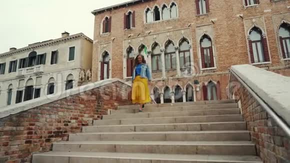 穿着黄色裙子的布鲁内特女孩在威尼斯运河大桥上走下楼梯视频的预览图