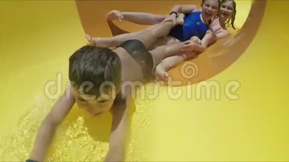 快乐的孩子们正在水上乐园里骑着黄色橙色的滑梯视频的预览图