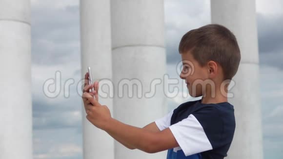 男孩在手机上对着天空和白色的柱廊自拍视频的预览图