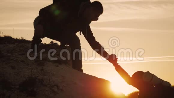 在两个登山者之间帮忙的剪影在山顶上有两个徒步旅行者一个男人帮助一个女人爬上一个纯粹的地方视频的预览图