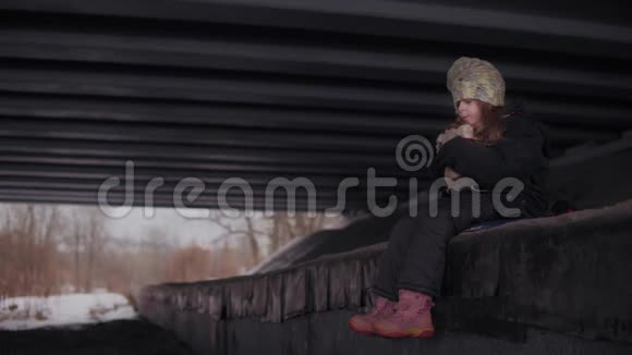 冬天无助的流浪儿童带着玩具坐在河边的桥下视频的预览图