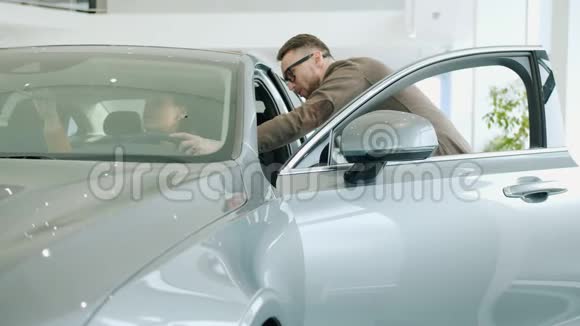 一位开朗的年轻女士在展厅检查汽车内部与推销员交谈视频的预览图