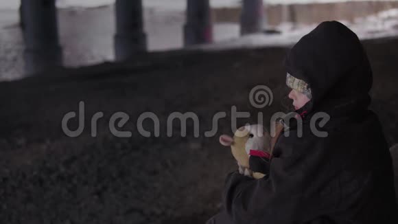 冬天无助的流浪儿童带着玩具坐在河边的桥下视频的预览图