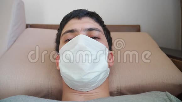 戴着医疗面具看着摄像机的人他躺在沙发上睡着了COVID19和2019年冠状病毒概念视频的预览图